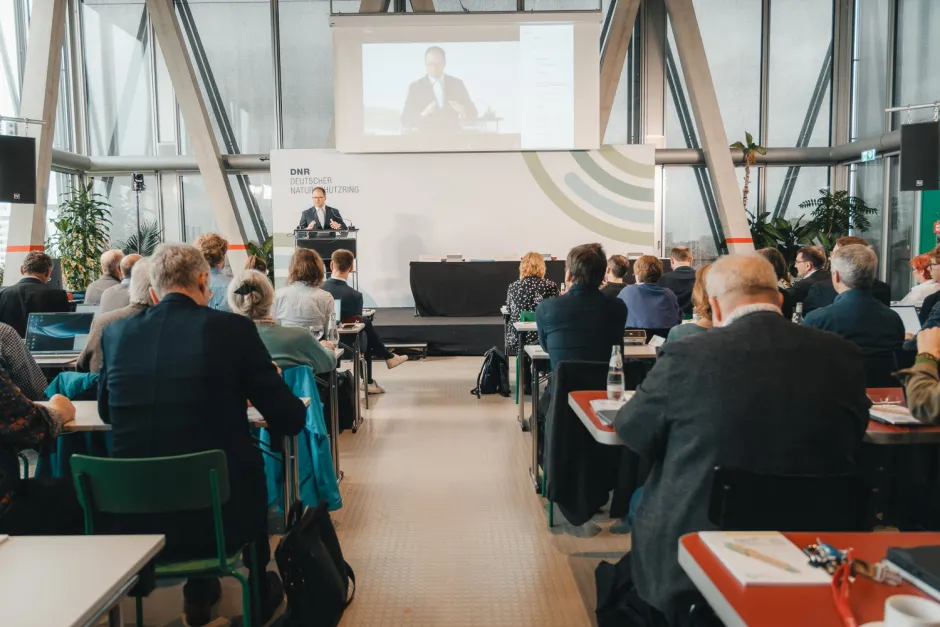 Blick in den Saal, vorne Carsten Schneider (Bundesumweltminister), der auch nochmal in groß als Bild auf der Leinwand im Hintergrund erscheint
